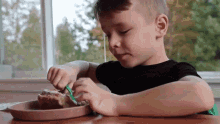 a young boy is sitting at a table eating a piece of food with a fork and knife .
