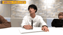 a man sitting at a table with a pen in his hand and a sign above him that says ' 1 week ' on it