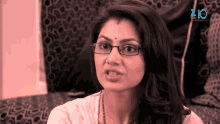 a woman wearing glasses is sitting on a couch in front of a screen that says 210