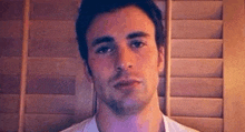 a young man with a beard is standing in front of a wooden wall .