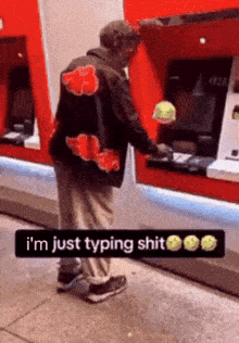 a man wearing a jacket that says i 'm just typing shit is using an atm machine