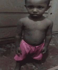 a shirtless young boy in pink shorts is standing in a room