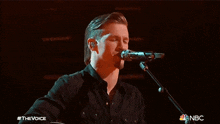 a man singing into a microphone with the nbc logo on the bottom right