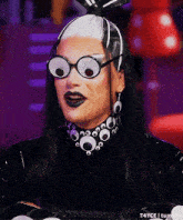 a drag queen wearing a black and white wig and glasses with googly eyes on her face .
