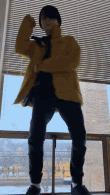 a person wearing a yellow jacket and black pants is standing in front of a window