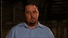 a man with a beard is wearing a blue shirt and making a funny face