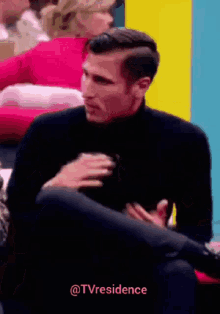 a man in a black turtleneck sits in front of a colorful wall with the words @tvresidence written below him