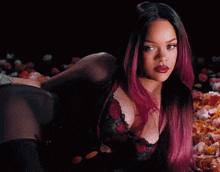 a woman with pink hair and red lips is laying on her stomach in front of a pile of flowers .