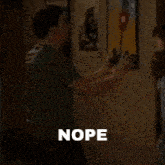 a man in a green shirt is standing in a room with the word nope written on the screen .