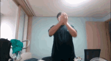 a man in a black shirt is standing in a room with his hands folded in front of his face