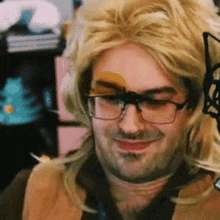 a man wearing glasses and a blonde wig smiles for the camera