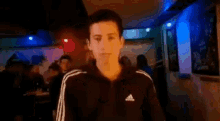 a man in a black adidas jacket is giving the middle finger in a dark room .