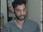 a man with a beard wearing a grey shirt looks at the camera