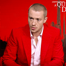 a man in a red jacket is sitting in front of a red background with the word aqui on it