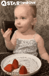 a little girl is sitting at a table eating strawberries from a white plate