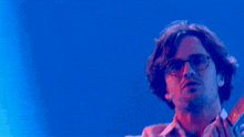 a man with glasses is playing a guitar in a blue light