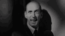 a bald man in a suit and tie is smiling in a black and white photo .