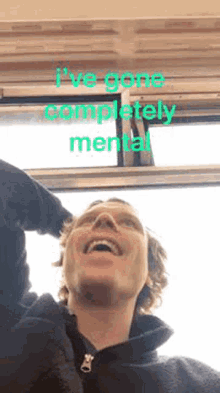 a man is laughing in front of a window with the words `` i 've gone completely mental '' written on it .