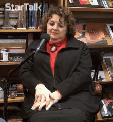 a woman sits in front of a microphone in front of a bookshelf with a book titled flight paths on it