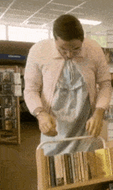 a man in a pink sweater and a blue dress is putting books on a shelf in a library .