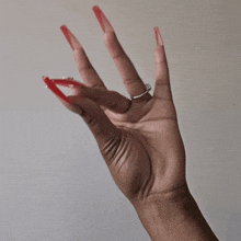 a woman 's hand with long red nails and a silver ring on her ring finger