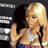 a woman with blonde hair and pink nails is standing on a red carpet with her hands up .