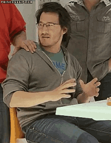 a man wearing glasses is sitting at a table with his hands outstretched
