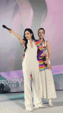 two women standing in front of a sign that says " proud to be "