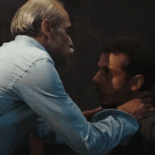two men are standing next to each other in a dark room . one of the men has a mustache .