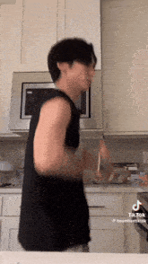 a young man in a black tank top is standing in a kitchen .