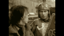 a man in armor is holding a shield in front of a woman in a black and white photo .