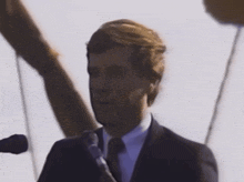 a man wearing a suit and tie is speaking into a microphone
