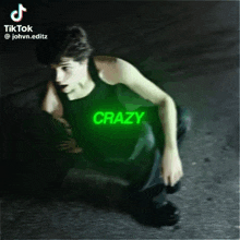 a young man in a black tank top is kneeling down with the word crazy glowing in the background .