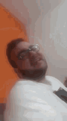 a man with a beard and glasses is sitting in front of an orange wall .