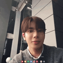 a young man wearing glasses and a gray sweater is looking at the camera