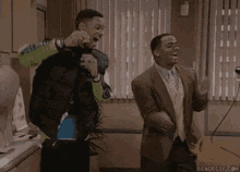 two men in suits are dancing in a kitchen .