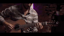 a close up of a person playing an acoustic guitar with a purple background