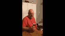 a man in a red shirt is sitting at a table holding a red cup .