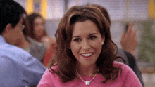 a woman in a pink sweater and necklace is smiling while sitting at a table with other people .