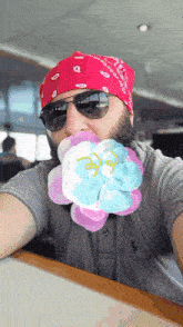 a man wearing a bandana and sunglasses has a flower in his mouth with the letter e on it
