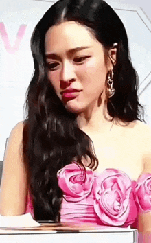 a woman with long black hair is wearing a pink dress with roses on it .
