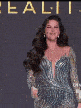 a woman in a blue dress is walking on a stage in front of a sign that says l reality