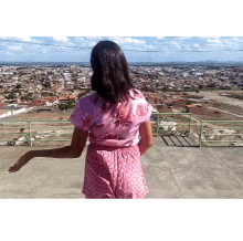 a woman in a pink top and shorts is standing on a balcony overlooking a city .