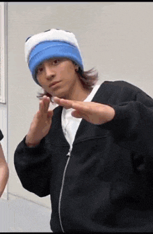 a man wearing a blue and white hat and a black jacket is making a peace sign with his hands .