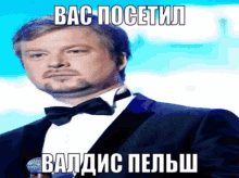 a man in a tuxedo and bow tie stands in front of a microphone with a foreign language caption