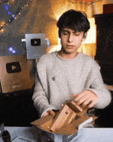 a young man in a grey sweater is opening a box with a youtube logo in the background