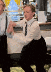 a woman in a white shirt and tie is dancing with a man in suspenders in front of a bar