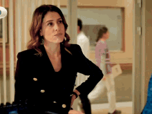 a woman in a black jacket is standing in a hallway with her hands on her hips