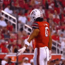 a football player wearing a red uniform and a white helmet is standing on a field .