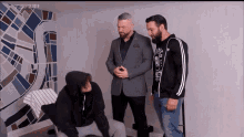 three men are standing next to each other in a room with a mural on the wall .
